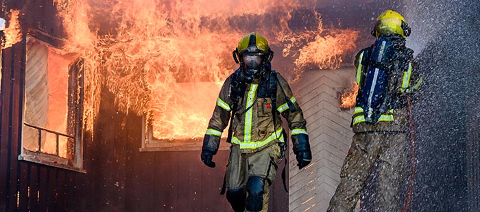 Zwei Feuerwehrleute die den Brandschaden eines Wohnhauses zu löschen versuchen