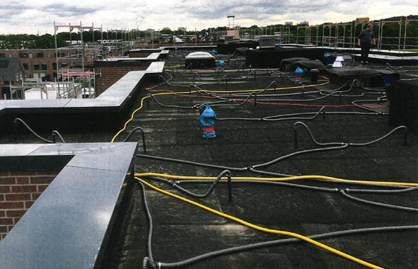 Technische Trocknung eines Flachdaches. Schläuche liegen quer über dem Dach verteilt und stecken im Flachdach